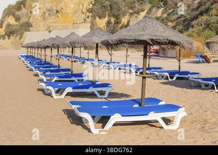 Rows of wicker beach parasols and blue beach beds Foto Stock