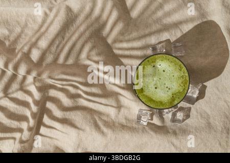 Scena estiva con latte matcha ghiacciato e ombra tropicale di foglie di palma su sfondo di lino color sabbia. Sole e ombre. Foto Stock