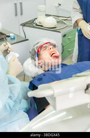L'adolescente mostra insoddisfazione mentre sdraiato su una sedia dentale, preparandosi per i trattamenti dentali in una clinica Foto Stock