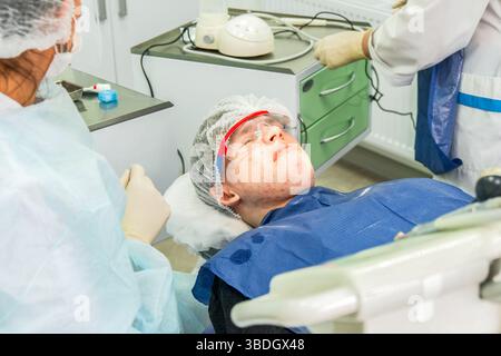 L'adolescente mostra insoddisfazione mentre sdraiato su una sedia dentale, preparandosi per i trattamenti dentali in una clinica Foto Stock