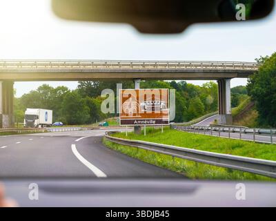 Francese, Francia - 24 agosto 2023: Vista dall'interno di un veicolo in movimento su un'autostrada che si avvicina a un cartello stradale turistico marrone per Amneville, con illustrazioni Foto Stock