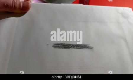 Parigi, Francia - 4 aprile 2025: Una mano regge la carta da imballaggio traslucida di un nuovo MacBook Pro con il testo in rilievo MacBook Pro reso visibile con un p Foto Stock