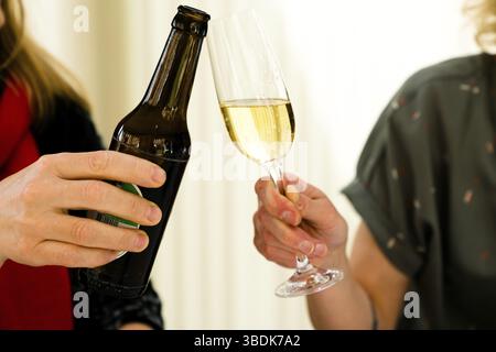 Vista in dettaglio di due donne che fanno un brindisi con una bottiglia di birra e un bicchiere di champagne Foto Stock