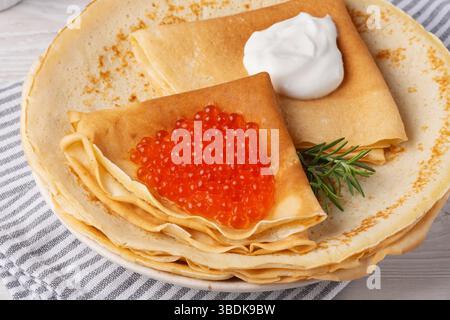 Deliziose crepes condite con caviale rosso servite su un accogliente tavolo alla luce del giorno Foto Stock