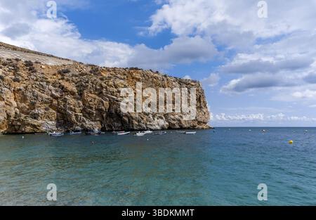 molte piccole barche colorate di legno da pesca ancorate in acque turchesi con una scogliera di arenaria alle spalle Foto Stock