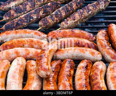 Salsicce e carne macinata su bastoncini di legno vengono cotte sulla griglia. Foto Stock