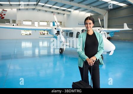 Studente pilota fiducioso in piedi con la valigia nell'hangar dell'aereo Foto Stock
