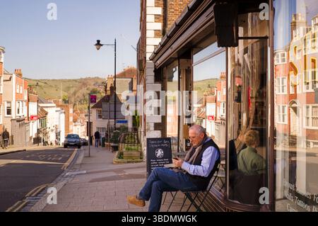 Un uomo anziano che guarda il telefono mentre si siede fuori da un bar a Lewes Foto Stock