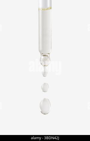 Vista ravvicinata dell'olio cosmetico che fuoriesce dalla pipetta su sfondo bianco. Foto Stock