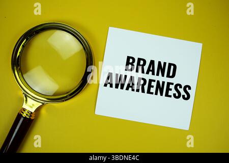 Messaggio di testo sulla brand awareness scritto su carta con vista dall'alto in vetro ingranditore su sfondo giallo Foto Stock