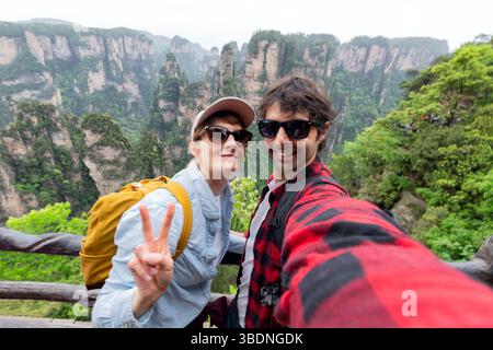 Una coppia di viaggiatori sta facendo un selfie con la vista sullo sfondo della scogliera calcarea di "Zhangjiajie". Qui c'è un incredibile punto di riferimento naturale della Cina. Foto Stock