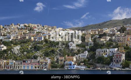 Case colorate tradizionali su una collina che si affaccia sulle acque cristalline del mare, Symi Town, Symi, Dodecaneso, Isole greche, Grecia, Europa Foto Stock