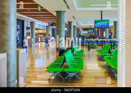 Spaziosa area d'attesa dell'aeroporto con sedie verdi, negozi duty free e passeggeri a piedi. Punta Cana. Repubblica Dominicana. Foto Stock