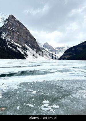 Il Lago Louise ghiacciato è circondato da montagne innevate sotto un cielo invernale nuvoloso, situato nel Parco Nazionale di Banff, Alberta, Canada. Foto Stock