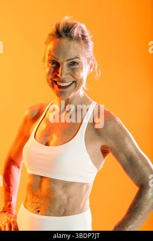 Bella donna sportiva matura che indossa abbigliamento sportivo per fare esercizio fisico - donna sportiva matura in abbigliamento atletico bianco che sorride con fiducia. Visualizzazione dell'abs a toni Foto Stock