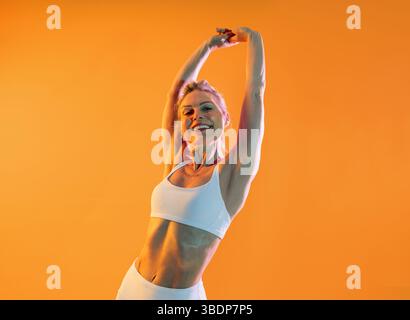 Bella donna sportiva matura che indossa abbigliamento sportivo per fare esercizio fisico - donna matura sportiva felice che indossa abbigliamento sportivo bianco si allunga le braccia e il sorriso Foto Stock