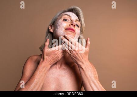 Ritratto di bellezza di una bella donna matura, concetti su cosmetici, cura della pelle e benessere. Donna matura che massaggia la crema idratante sul viso e Foto Stock