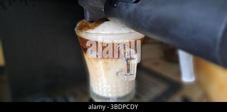 Macchina per il caffè per preparare un delizioso cappuccino con latte e panna in una tazza di vetro Foto Stock