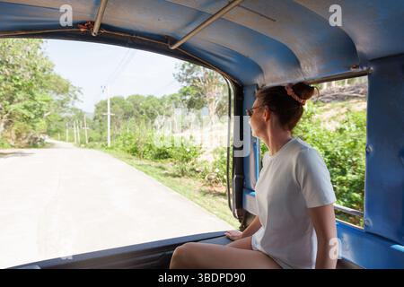 Un viaggiatore gode di un giro in tuk-tuk attraverso la lussureggiante campagna della Thailandia. Il sole splende brillantemente mentre guarda il paesaggio panoramico, catturando Foto Stock
