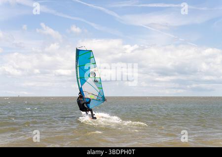 Swale Sittingbourne, Regno Unito. 25 maggio 2025. Tempo nel Regno Unito: Domenica soleggiata lungo la costa del Kent: Con una leggera brezza in aria, i windsurf si tuffano in acqua su tavole a vela mentre gli amanti della spiaggia si crogiolano nel calore del sole pomeridiano. Un vivace mix di relax e avventura mentre la scena costiera prende vita Credit: xiu bao/Alamy Live News Foto Stock