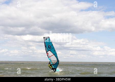 Swale Sittingbourne, Regno Unito. 25 maggio 2025. Tempo nel Regno Unito: Domenica soleggiata lungo la costa del Kent: Con una leggera brezza in aria, i windsurf si tuffano in acqua su tavole a vela mentre gli amanti della spiaggia si crogiolano nel calore del sole pomeridiano. Un vivace mix di relax e avventura mentre la scena costiera prende vita Credit: xiu bao/Alamy Live News Foto Stock