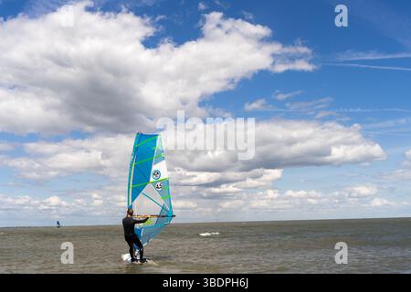 Swale Sittingbourne, Regno Unito. 25 maggio 2025. Tempo nel Regno Unito: Domenica soleggiata lungo la costa del Kent: Con una leggera brezza in aria, i windsurf si tuffano in acqua su tavole a vela mentre gli amanti della spiaggia si crogiolano nel calore del sole pomeridiano. Un vivace mix di relax e avventura mentre la scena costiera prende vita Credit: xiu bao/Alamy Live News Foto Stock