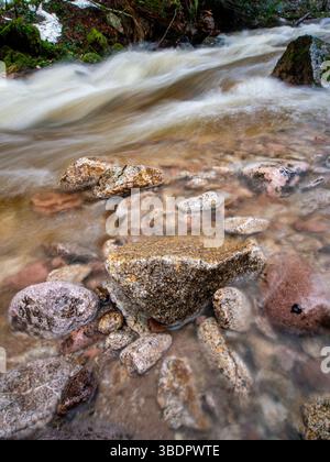 Le cascate d'acqua precipitano su rocce arrotondate in un fiume, creando un'atmosfera tranquilla. La foresta circostante presenta una vegetazione vibrante, che migliora il Foto Stock