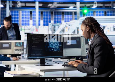Operaio che scrive codice IA presso la workstation in un impianto fotovoltaico, creando strumenti di manutenzione predittiva. Ingegneri che utilizzano l'intelligenza artificiale per analizzare i modelli di produzione e apportare miglioramenti Foto Stock