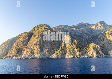 Costa panoramica vicino alla fine della Gola di Samaria, caratterizzata da aspre scogliere con pendii boscosi e calme acque turchesi, catturando la bellezza selvaggia di Cre Foto Stock
