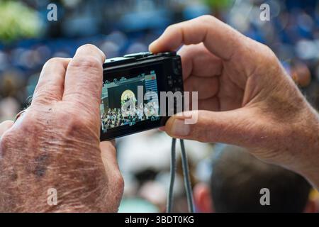 American Fork, UT, USA – 24 maggio 2025: Un individuo anziano registra una cerimonia di laurea presso un'accademia di American Fork, Utah, utilizzando una fotocamera digitale. Foto Stock