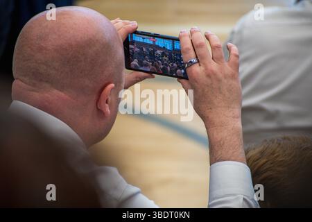 American Fork, UT, USA – 24 maggio 2025: Un uomo registra una cerimonia di laurea sul suo smartphone presso un'accademia di American Fork, catturando un momento speciale. Foto Stock