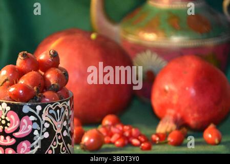 Natura morta in stile orientale: Melograni, caraffa, rosa fianchi maturi, mela rossa. Frammento Foto Stock