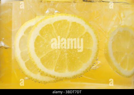 Acqua rinfrescante con fette di limone e ghiaccio in vetro su sfondo giallo, primo piano Foto Stock