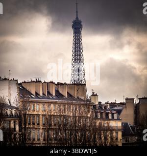 Con un suggestivo cielo coperto, la Torre Eiffel si innalza in modo impressionante sopra gli edifici storici di Parigi. Francia Foto Stock