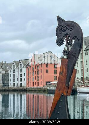 La testa vichinga di un ornamento di prua della nave attraccata nel canale Brosundet, con i colorati edifici in stile Art Nouveau di Alesund, Norvegia, che si riflettono nella calma Foto Stock