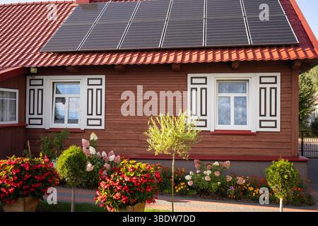 Una casa con tetto rosso e finiture bianche. La casa ha una grande finestra sul davanti e una piccola finestra sul lato. La casa ha un grande giardino con fl Foto Stock
