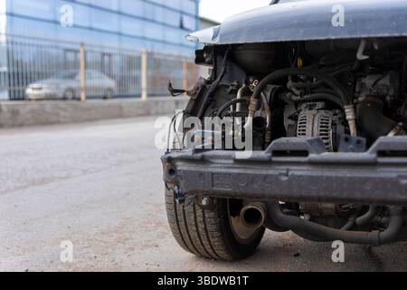 Veicolo danneggiato con paraurti anteriore mancante, che rivela i componenti del motore, il cablaggio e il telaio su una strada urbana. Foto Stock