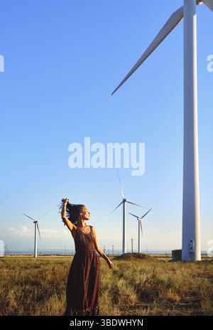 Donna elegante che balla nel campo con le turbine eoliche Foto Stock