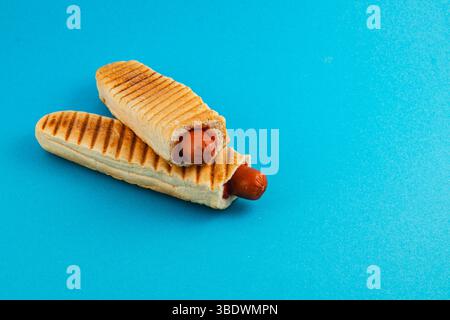 Two grilled hot dogs are nestled in toasted, golden-brown buns, resting on a vibrant blue surface, showcasing a simple yet appealing snack. Foto Stock
