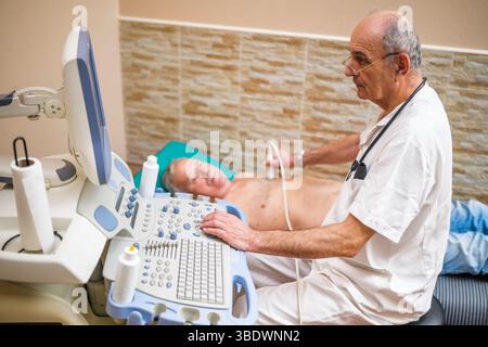 Uomo anziano che ha un esame medico. Il paziente anziano sta effettuando un esame ecografico del suo cuore da parte di un medico esperto. Foto Stock