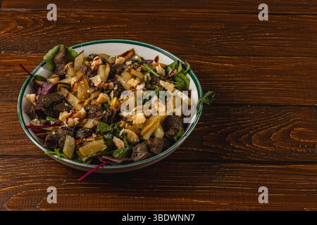 Una vibrante insalata con carne cotta, verdure assortite e noci è presentata in una grande ciotola su un rustico tavolo di legno, che mostra un pasto sano Foto Stock