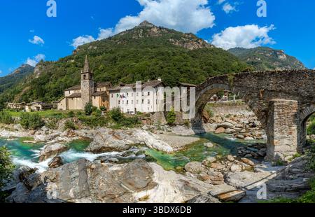 Panorama di un vecchio ponte in pietra su un fiume alpino con rocce, come una piccola chiesa si erge su una montagna sullo sfondo a Lillianes, Italia. Foto Stock