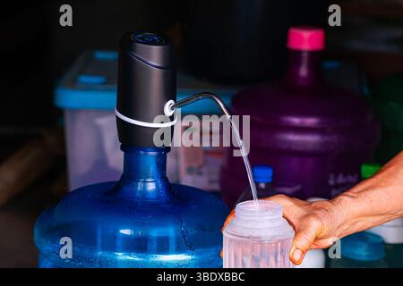 Bottiglia di plastica di riempimento manuale femmina con acqua trasparente proveniente dalla mini pompa elettrica portatile. Foto Stock