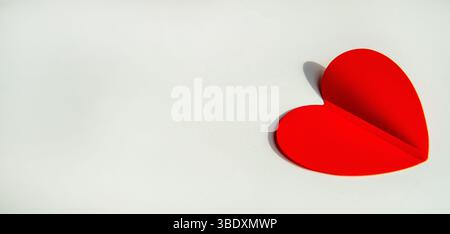 Striscione con decorazione in carta a forma di cuore rosso su sfondo bianco. Piano, vista dall'alto, spazio per il testo sul lato sinistro. Foto Stock