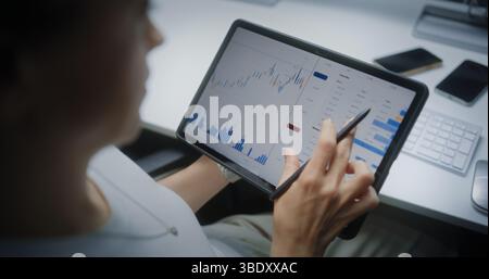 Broker di borsa femminile monitoraggio e analisi delle azioni in tempo reale, grafici di mercato nell'app di trading online con tablet e stilo digitali. Agente di investimento professionale che lavora in ufficio. Primo piano. Foto Stock