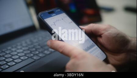 Uomo che controlla le azioni in tempo reale e i grafici del mercato di Exchange su smartphone e laptop, guarda la lezione di trading online su tablet. Dipendenti che effettuano investimenti durante l'orario di lavoro in officina. Primo piano. Foto Stock