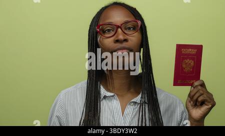 Donna con passaporto russo su sfondo giallo che indossa occhiali e camicia a righe, raffigurante concetti di viaggio e identità. Foto Stock