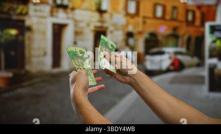 Uomo che tiene in mano banconote in rand sudafricano in una vivace strada urbana, illustrando le transazioni finanziarie e il cambio valuta in una città all'aperto Foto Stock