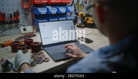 Uomo che controlla azioni in tempo reale, grafici Exchange Market utilizzando un computer portatile. Dipendente che effettua investimenti in criptovaluta durante l'orario di lavoro in officina, combinando lavoro e Trading online. Primo piano. Foto Stock