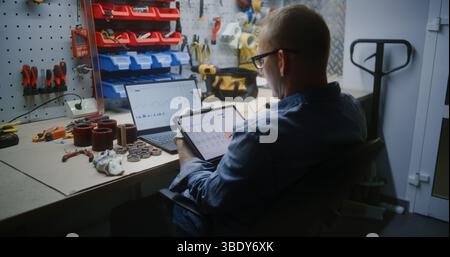 Dipendenti che controllano azioni in tempo reale e grafici Exchange Market utilizzando tablet e laptop digitali. Uomo che effettua investimenti in criptovaluta durante l'orario di lavoro in Workshop, combinando lavoro e Trading online Foto Stock